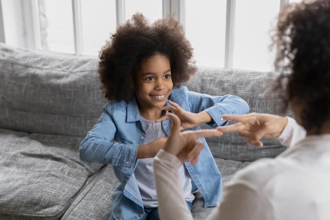 A child playing a game with their hands with an adult's hands doing the same in the foreground