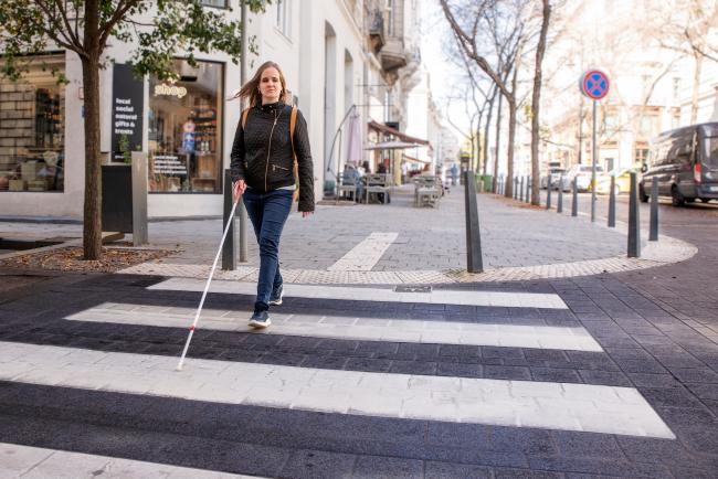 A person crossing a street in a crosswalk with the aid of a white cane